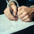 Hands in handcuffs holding a pen above a legal document. Hands in handcuffs holding a pen above a legal document.