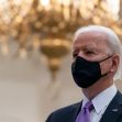 Joe Biden speaking during an event, wearing a mask, with a chandelier in the background. Joe Biden speaking during an event, wearing a mask, with a chandelier in the background.