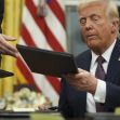Former President Donald Trump signs documents in the Oval Office, surrounded by the U.S. flag and other symbols of his administration. Former President Donald Trump signs documents in the Oval Office, surrounded by the U.S. flag and other symbols of his administration.
