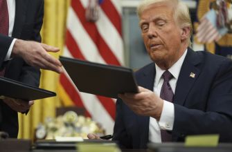 Former President Donald Trump signs documents in the Oval Office, surrounded by the U.S. flag and other symbols of his administration.