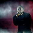 Kendrick Lamar performing on stage with a microphone in hand, surrounded by smoke and dramatic lighting. Kendrick Lamar performing on stage with a microphone in hand, surrounded by smoke and dramatic lighting.