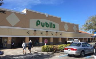 Publix store exterior with customers and parked cars.