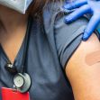 A close-up of a person receiving a vaccination, showing their arm with a bandage and a healthcare professional's gloved hand administering the shot. A close-up of a person receiving a vaccination, showing their arm with a bandage and a healthcare professional's gloved hand administering the shot.