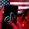 A hand holding a smartphone displaying the TikTok logo, set against the backgrounds of the American and Chinese flags. A hand holding a smartphone displaying the TikTok logo, set against the backgrounds of the American and Chinese flags.