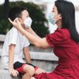 A woman helps a young boy put on a protective face mask outdoors. A woman helps a young boy put on a protective face mask outdoors.