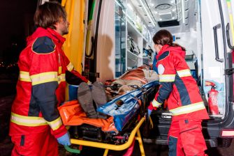 Paramedics loading a patient onto a stretcher in an ambulance during a medical emergency.