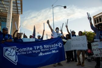 A rally supporting Temporary Protected Status (TPS) with demonstrators holding signs and a banner in Las Vegas.