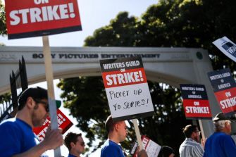 Writers Guild members holding signs during a strike, demanding better wages and protections against AI in front of Sony Pictures Entertainment.