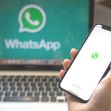 A person holding a smartphone displaying the WhatsApp logo, with a laptop in the background also showing the WhatsApp logo. A person holding a smartphone displaying the WhatsApp logo, with a laptop in the background also showing the WhatsApp logo.