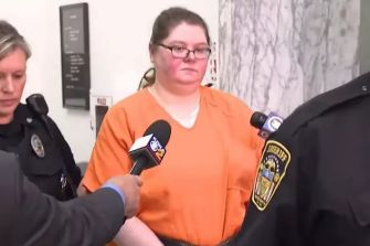 Former nurse Heather Pressdee in an orange prison jumpsuit during a court proceeding, surrounded by law enforcement officers.