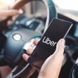 A person holding an Uber app on a smartphone while driving a car. A person holding an Uber app on a smartphone while driving a car.