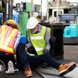 A workplace accident scene with two safety personnel attending to an injured worker on the floor. A workplace accident scene with two safety personnel attending to an injured worker on the floor.