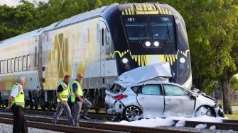 A damaged car after a collision with a Brightline train, with emergency responders on the scene.