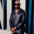 A man wearing sunglasses and a stylish black outfit poses confidently, with a serious expression, against a modern, blue-patterned background. A man wearing sunglasses and a stylish black outfit poses confidently, with a serious expression, against a modern, blue-patterned background.