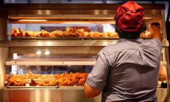 A fast food worker serving food from a display case in a restaurant kitchen.