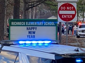 Sign outside Richneck Elementary School displaying "HAPPY NEW YEAR" with police presence in the foreground.
