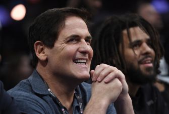 Mark Cuban smiling while seated at an event, accompanied by another individual.