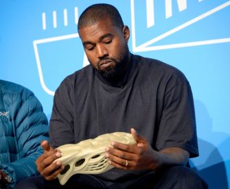 Kanye West examining a Yeezy Foam Runner shoe during a presentation.