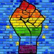 A raised fist symbol with a rainbow gradient against a blue brick wall, representing LGBTQ+ rights and activism. A raised fist symbol with a rainbow gradient against a blue brick wall, representing LGBTQ+ rights and activism.