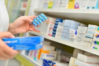 A person holding a blister pack of medication in a pharmacy, with various pharmaceutical boxes in the background.