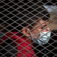 A young boy wearing a mask is seen behind a metal grid, highlighting the conditions faced by unaccompanied minors at the U.S. southern border. A young boy wearing a mask is seen behind a metal grid, highlighting the conditions faced by unaccompanied minors at the U.S. southern border.