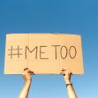A person holding a cardboard sign that reads "#Me Too" against a blue sky. A person holding a cardboard sign that reads "#Me Too" against a blue sky.