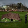 A person walks past a tent set up on a grassy area, indicating the presence of homelessness. A person walks past a tent set up on a grassy area, indicating the presence of homelessness.