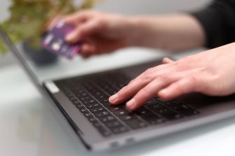 Close-up of a person's hand using a laptop keyboard while holding a credit card.