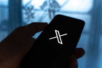 A person holding a smartphone displaying the X app interface on the screen.