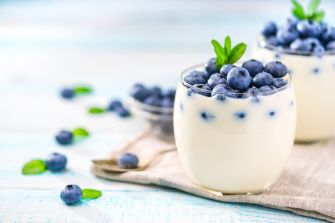 A serving of yogurt topped with blueberries and mint leaves, placed on a light blue wooden surface.