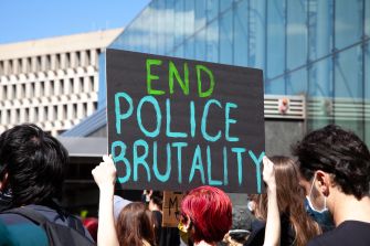 Sign at a protest reading "END POLICE BRUTALITY" with participants in the background.