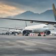 A row of airplanes parked on a runway with mountains in the background. A row of airplanes parked on a runway with mountains in the background.