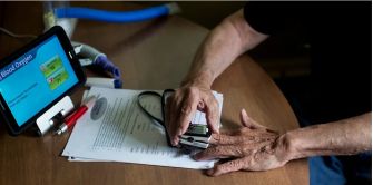 A person using a medical device to check their blood oxygen levels, surrounded by paperwork and a tablet displaying health information.