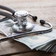 A stethoscope resting on a pile of hundred-dollar bills on a wooden surface. A stethoscope resting on a pile of hundred-dollar bills on a wooden surface.