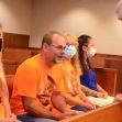 Family members sitting in a courtroom, some in orange shirts, engaging with a lawyer during a wrongful death lawsuit hearing. Family members sitting in a courtroom, some in orange shirts, engaging with a lawyer during a wrongful death lawsuit hearing.