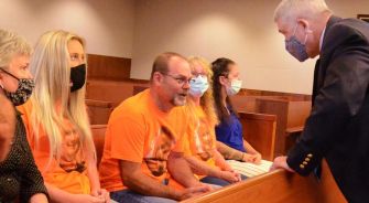 Family members sitting in a courtroom, some in orange shirts, engaging with a lawyer during a wrongful death lawsuit hearing.
