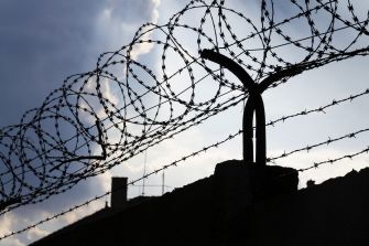 Barbed wire on a prison wall against a cloudy sky.