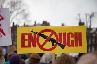 A protest sign reads "ENOUGH" with an image of a gun crossed out, symbolizing opposition to gun violence.