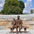 A bronze statue depicting Abraham Lincoln seated on a bench with a young boy, set against a stone wall inscribed with the phrase "To Bind Up the Nation's Wounds." A bronze statue depicting Abraham Lincoln seated on a bench with a young boy, set against a stone wall inscribed with the phrase "To Bind Up the Nation's Wounds."