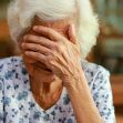 An elderly woman with white hair covering her face with one hand, expressing distress or concern. An elderly woman with white hair covering her face with one hand, expressing distress or concern.