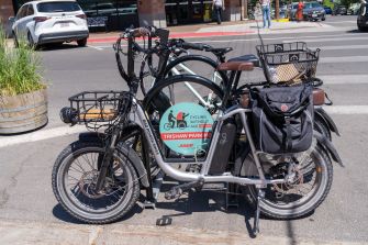 A close-up of electric bikes parked in an urban setting, featuring a prominent logo on one of the bikes.