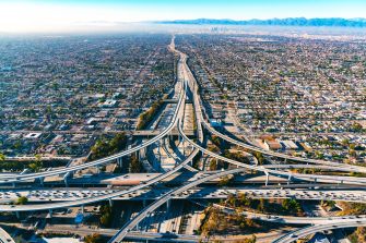 Aerial view of a sprawling highway system with traffic and a city skyline in the background.