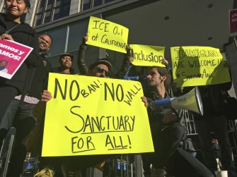 Protesters holding signs advocating for sanctuary cities and against immigration enforcement policies.