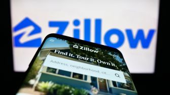 Smartphone displaying Zillow's real estate platform with the company's logo in the background.