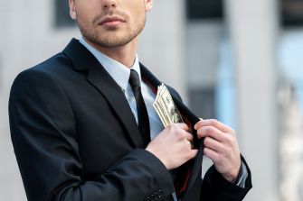 A man in a suit placing cash into his jacket pocket, symbolizing embezzlement.