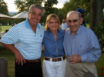 A group of three people posing outdoors, smiling, at a social gathering.