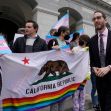 A group of LGBTQ activists holding a California state flag with a rainbow stripe and signs advocating for LGBTQ rights outside a government building. A group of LGBTQ activists holding a California state flag with a rainbow stripe and signs advocating for LGBTQ rights outside a government building.