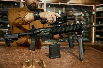 A person assembling a firearm with ammunition displayed on a table in a gun store or workshop.