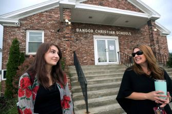 Two women stand outside Bangor Christian Schools, discussing in front of the entrance.