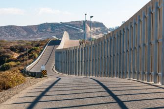 View of the border wall in a landscape setting, showcasing the structure's height and surrounding terrain.